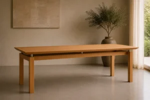 Ein minimalistischer Esstisch aus Holz in einem hellen Raum mit einer großen Vase voller Grünpflanzen neben einem Fenster.